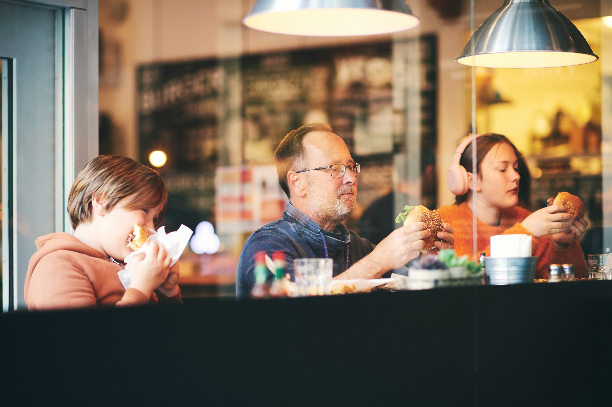 Family lunch, father with children eating hamburgers, in restaurant, sitting by the window