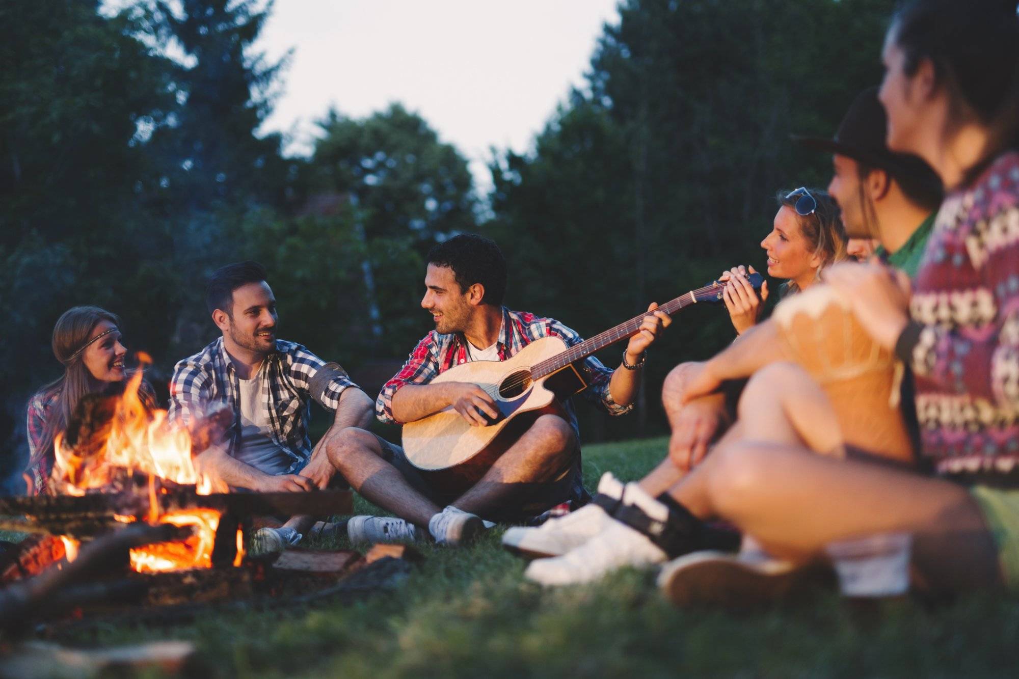 Happy friends playing music and enjoying bonfire in nature Happy friends playing music and enjoying bonfire in nature