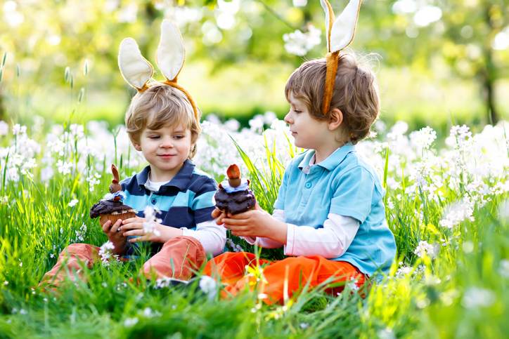Two little boy friends in Easter bunny ears eating chocolate cakes and muffins Two little boy friends in Easter bunny ears eating chocolate cakes and muffins