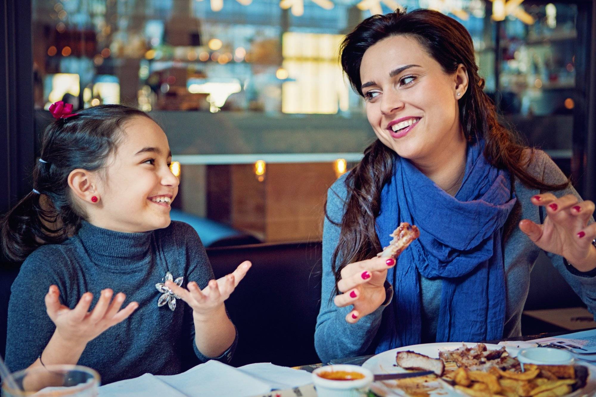 Mother and daughter are eating pork ribs in the restaurant with hands