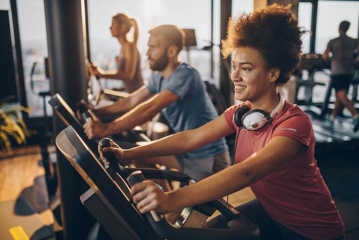 Happy black athlete practicing on exercise bike in a health club.